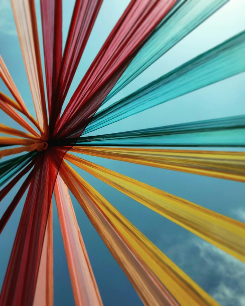 Colorful textile art installation reaching towards a clear blue sky, showcasing vibrant hues and creativity.